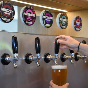 Person pouring Sprig + Fern beer from a tap into a proper pint glass, with other beer taps and labels in the background.