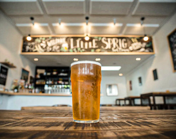 Pint of Sprig + Fern beer on a bar counter with 'Little Sprig' sign in the background