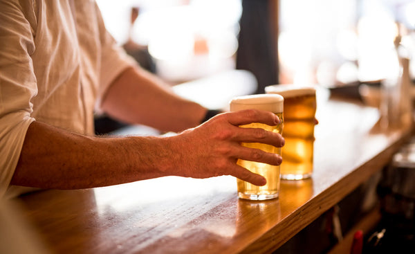 Person holding two Proper Pints of beer at the bar of Sprig + Fern Hardy Street.