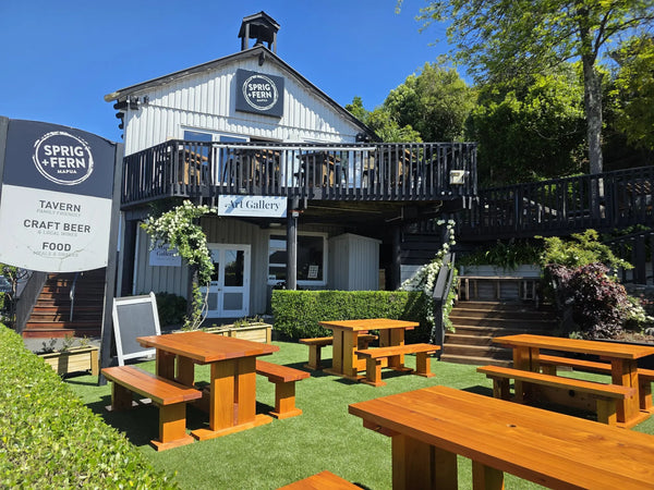 Outdoor seating area with wooden tables and benches in front of Sprig + Fern Mapua Tavern.
