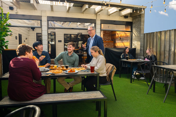 Group of people dining outdoors in a modern patio area at Sprig + Fern Petone.