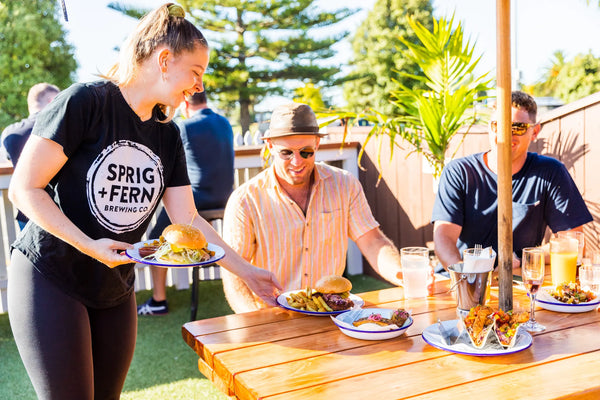 People enjoying food and drinks at the Sprig + Fern Tahuna Tavern with a focus on a person holding a plate of food.
