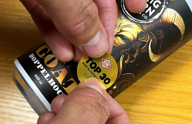 A New World Beer and Cider Awards medal sticker being applied to a can of Sprig and Fern's The G.O.A.T Doppelbock